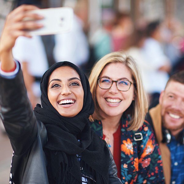 happy muslim woman taking photo with friends using 7CJGV35